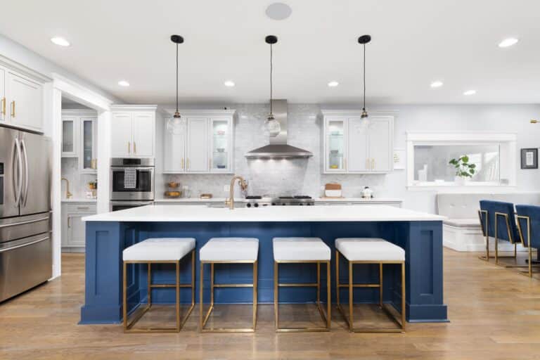 A beautiful modern kitchen with grey and blue cabinets, stainless steel Viking appliances, gold hardware and glass lights hanging above the large island.